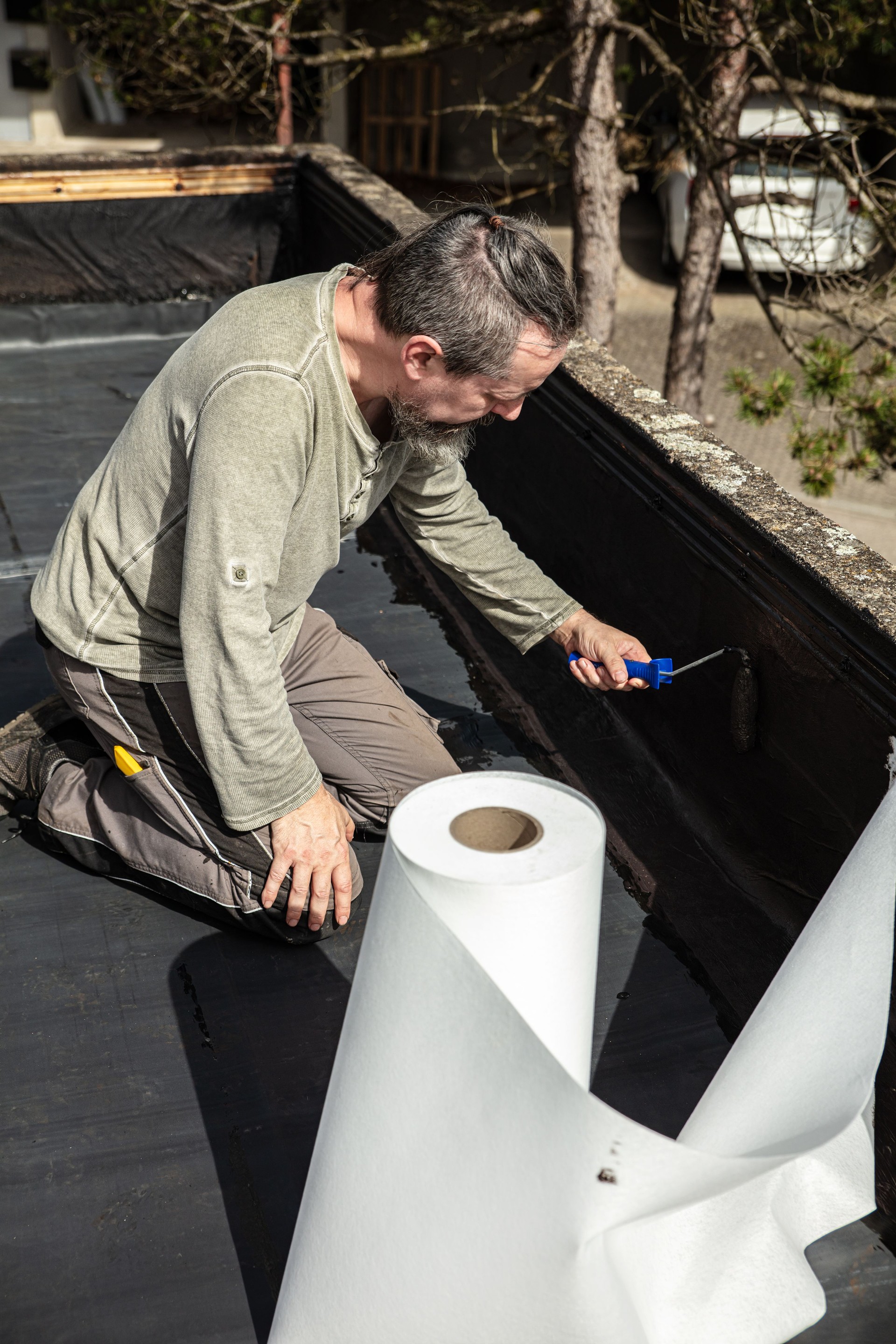 a craftsman applies liquid bitumen to a roof to seal it